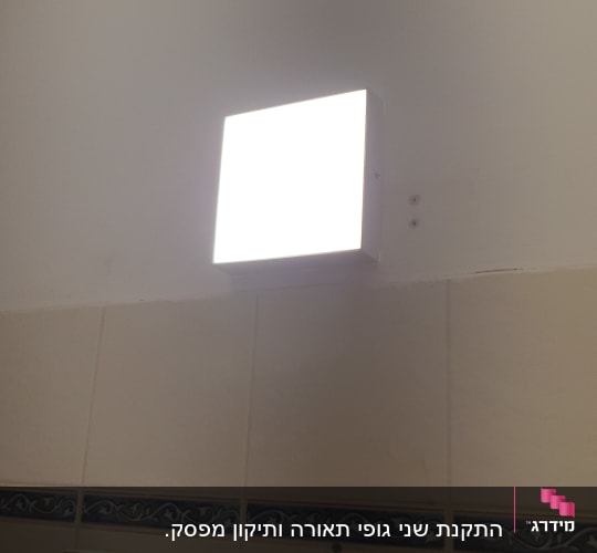 מנורת קיר מרובעת מוארת על קיר לבן